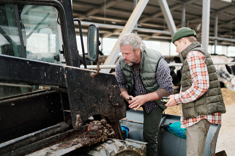 Two men engaged in a discussion while inspecting a tractor, focusing on repair and maintenance.