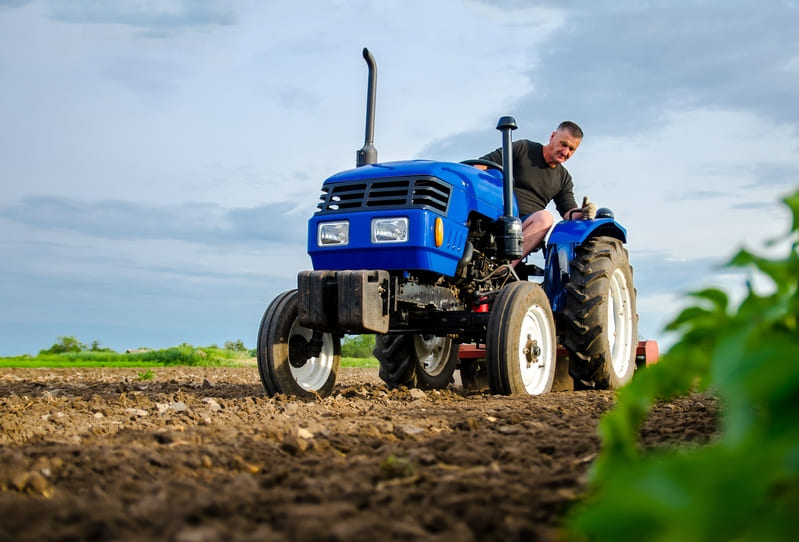 A 2WD farm tractor plowing a field, showcasing its robust design and agricultural utility in action.