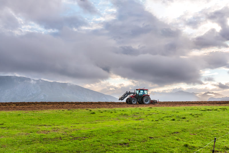 A farm tractor plowing a field, showcasing agricultural activity and rural landscape.