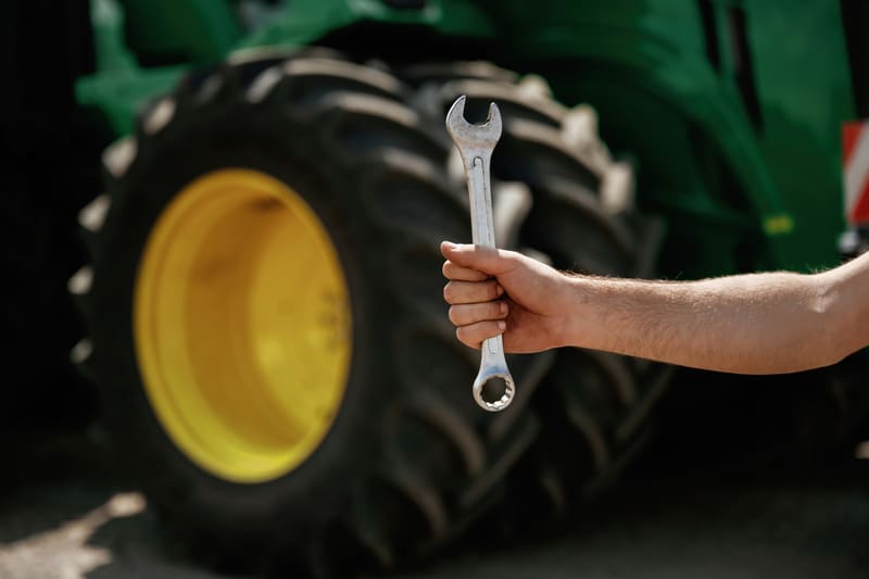 A collection of farm tractor repair tools, including wrenches, sockets, and pliers, organized on a workbench.