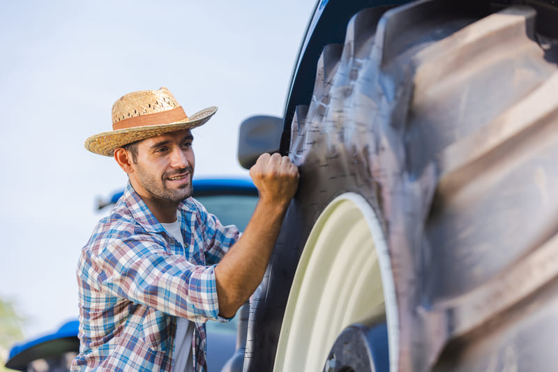 A farmer inspects the condition of a tractor in a field, ensuring it is ready for agricultural work.