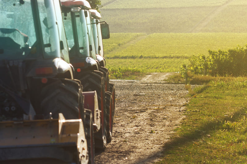 A row of tractors working in a vast agricultural field under a clear blue sky, showcasing modern farming equipment.