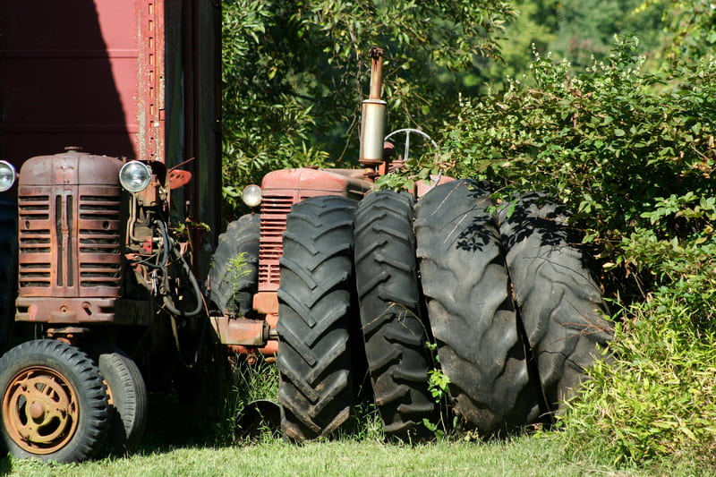 Worn farm tractor tires showing significant tread wear and weathering, indicating extensive use in agricultural activities.