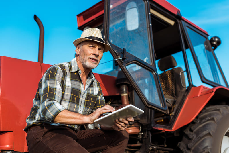 A farmer performing maintenance on a farm tractor, checking fluids, inspecting tires, and cleaning the engine.