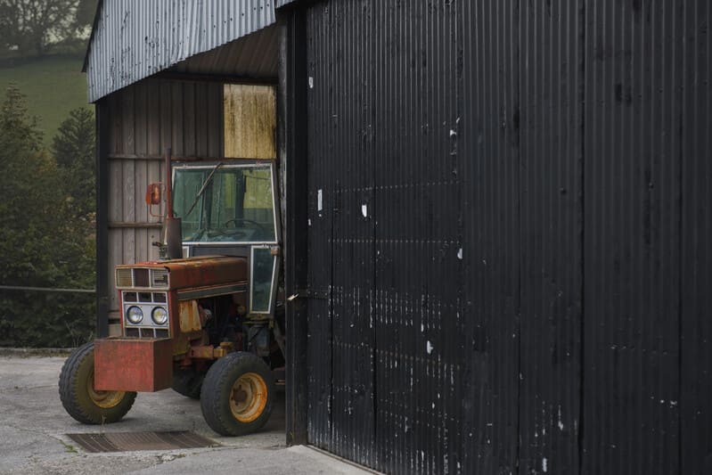 A farm tractor parked inside a barn, protected from weather and ready for future use.