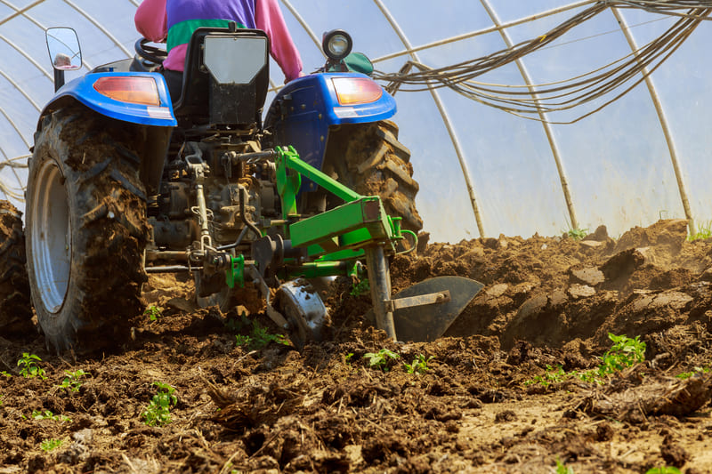 A farm tractor equipped with a plow attachment, turning over soil to prepare the field for planting.