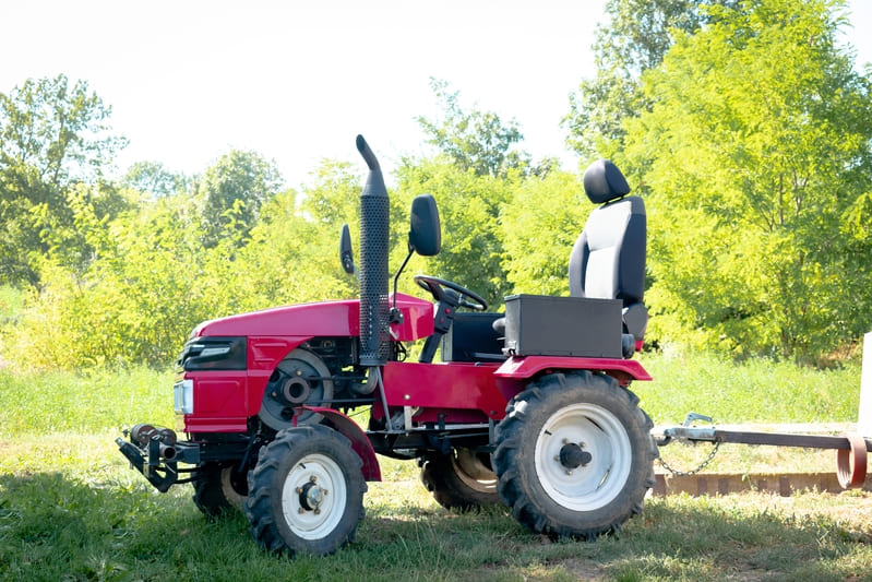 A red utility tractor parked on a grassy field, ready for versatile farming tasks.