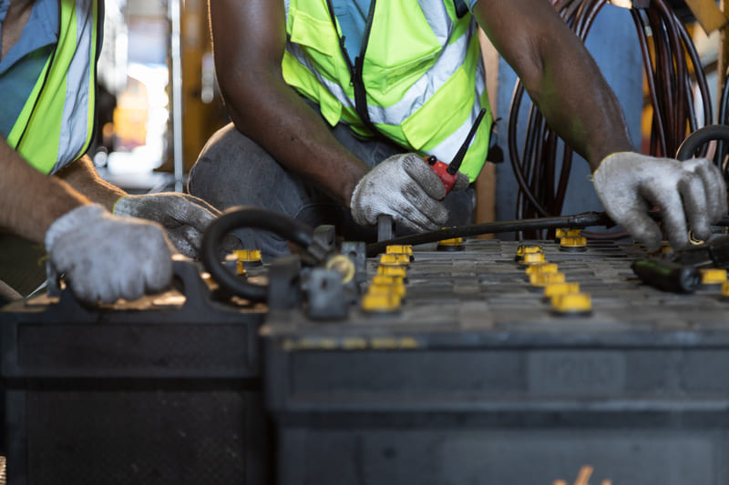 A farmer inspecting and maintaining a tractor battery to ensure reliable engine starts and electrical performance.