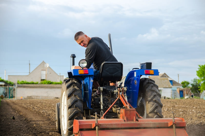 A farmer conducting a pre-use inspection on a tractor, checking fluids, tires, and safety features.