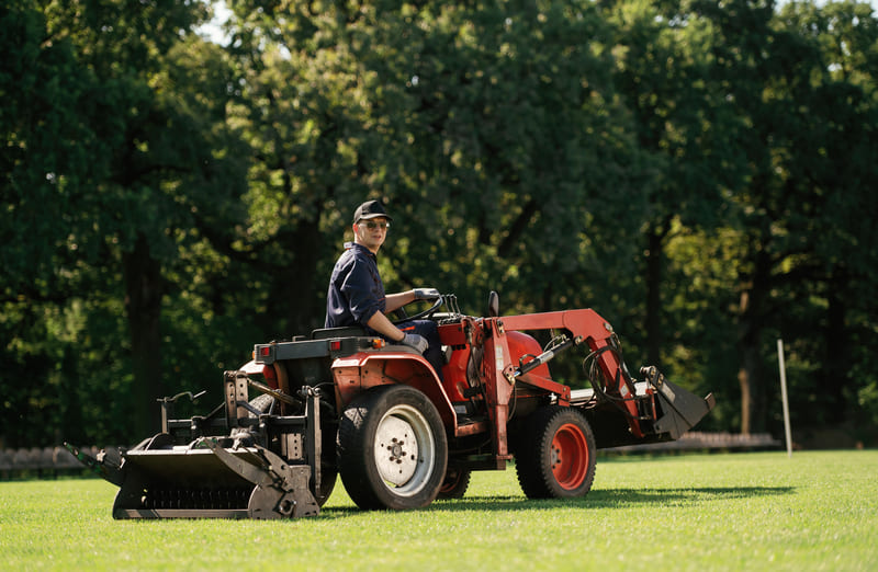 A utility tractor equipped with a grass cutter attachment, trimming a large grassy field.