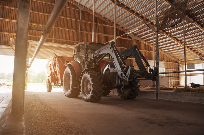A farm tractor parked in a covered storage shed, protected from the elements to preserve its condition and performance.