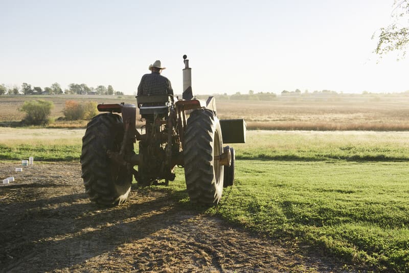 A modern farm tractor equipped with safety devices including ROPS, seatbelt, mirrors, lights, and slow-moving vehicle signage.