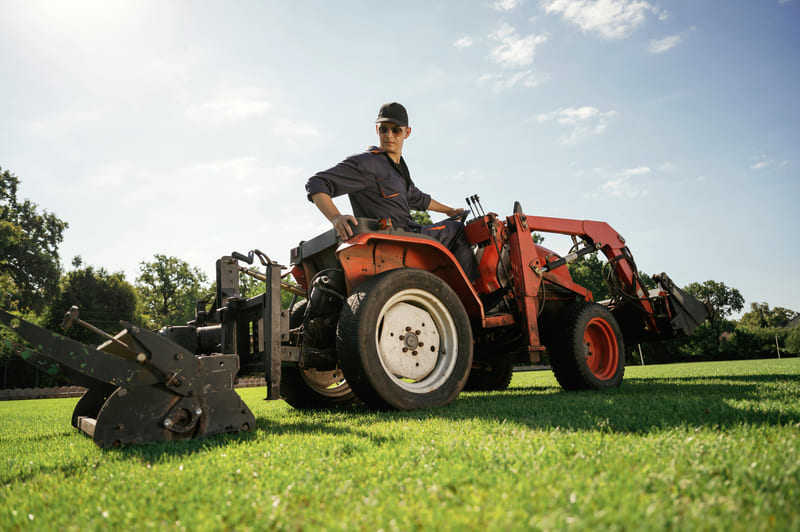A farm tractor equipped with a front-end loader lifting a pile of soil, ideal for heavy-duty agricultural tasks.