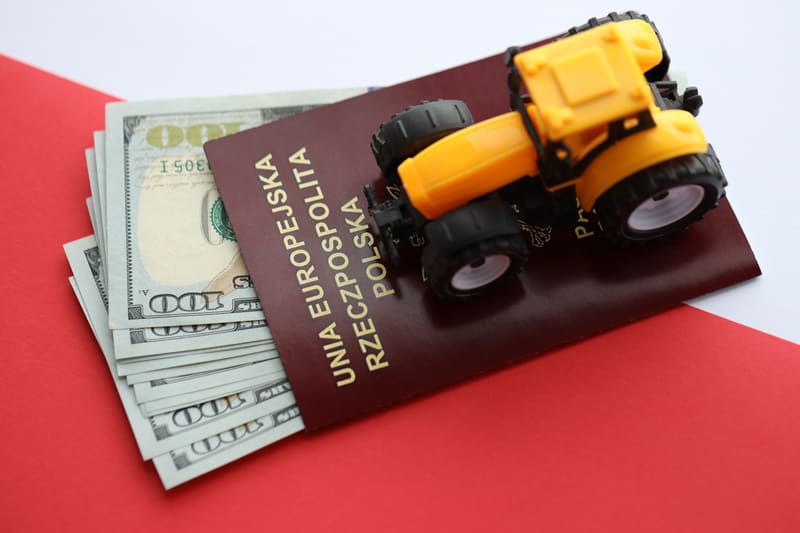 Stacks of coins and dollar bills next to a farm tractor, symbolizing the financial investment required to own and operate agricultural machinery.
