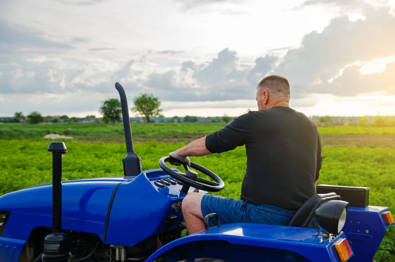 A compact farm tractor working in a small field, equipped with a front-end loader and turf-friendly tires for light-duty agricultural tasks.