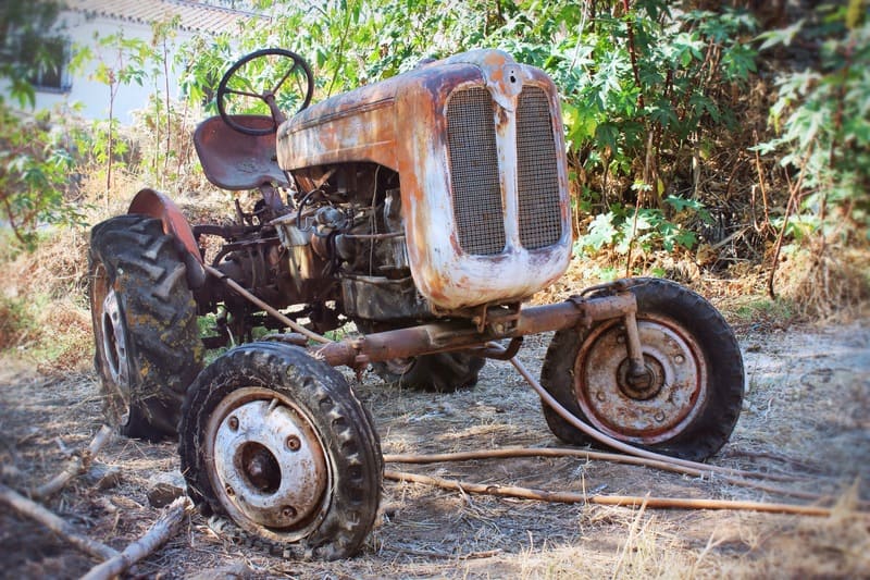 An old farm tractor resting near a barn, with faded paint and visible wear, symbolizing its years of service on the land.