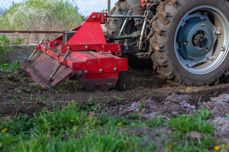 Compact tractor with rotary tiller attached preparing soil in a small farm, ideal for efficient land cultivation.